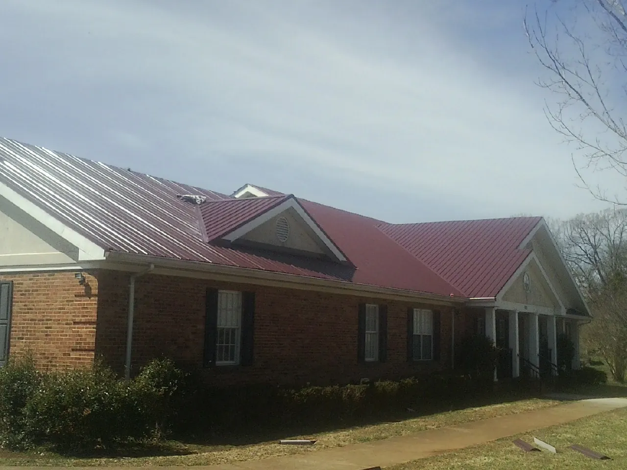 Red metal roof with gabled entries on a long brick building, from a Hail Damage Roof Repair job in Washburn