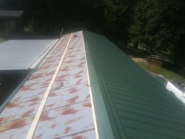 Old rusted panels beside newly installed green metal roofing — Wind Damage Roof Repair by Roofing Brothers in Washburn