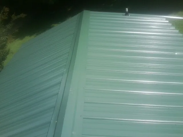 New green metal panels meeting at the ridge of a roof — Flat Roof Repair work by our crew in Washburn